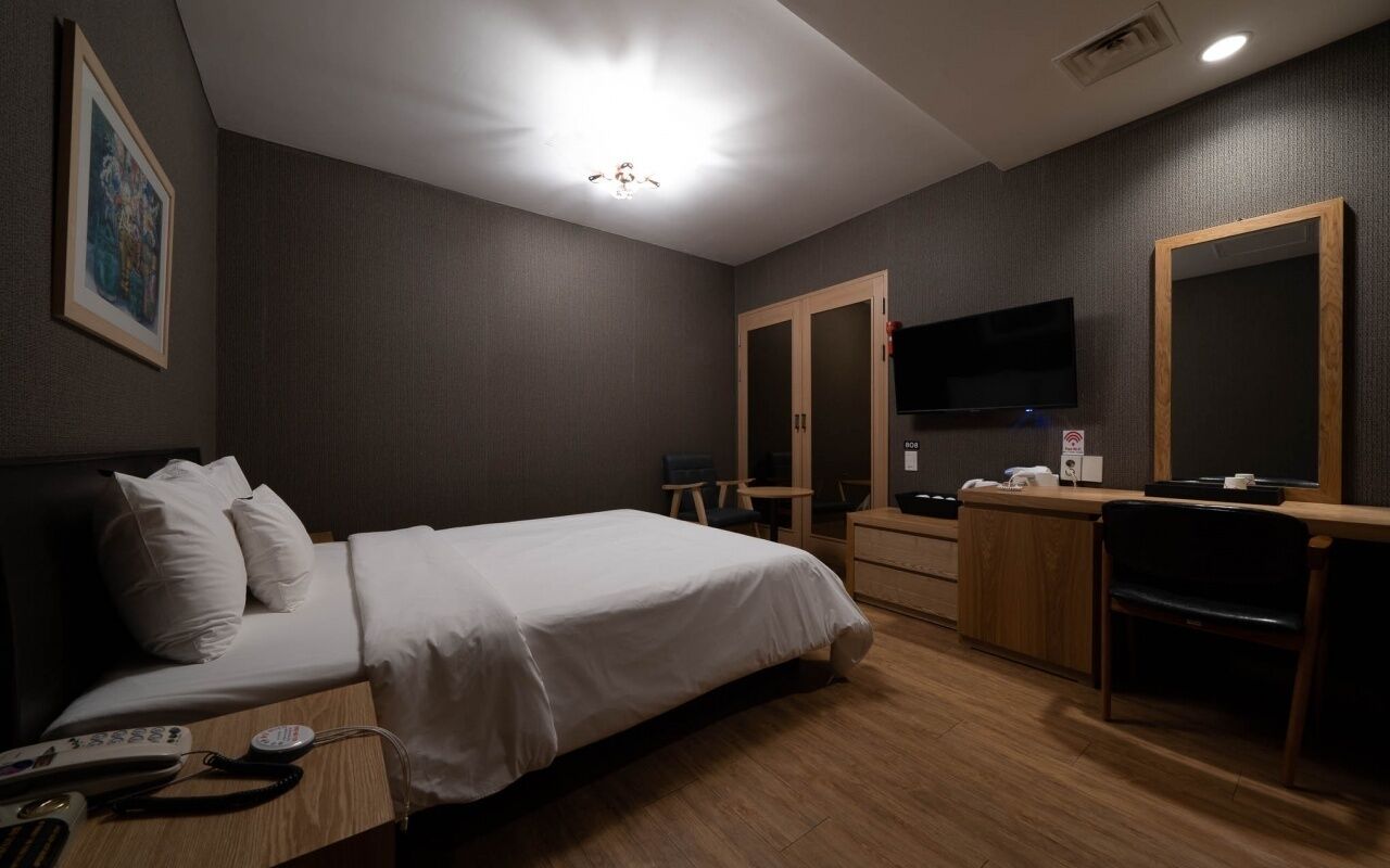 A hotel room with a bed, bedside table, desk, chair, TV, and wardrobe.