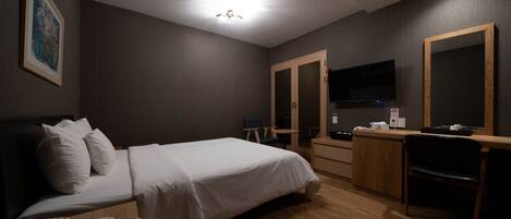 A hotel room with a bed, bedside table, desk, chair, TV, and wardrobe.