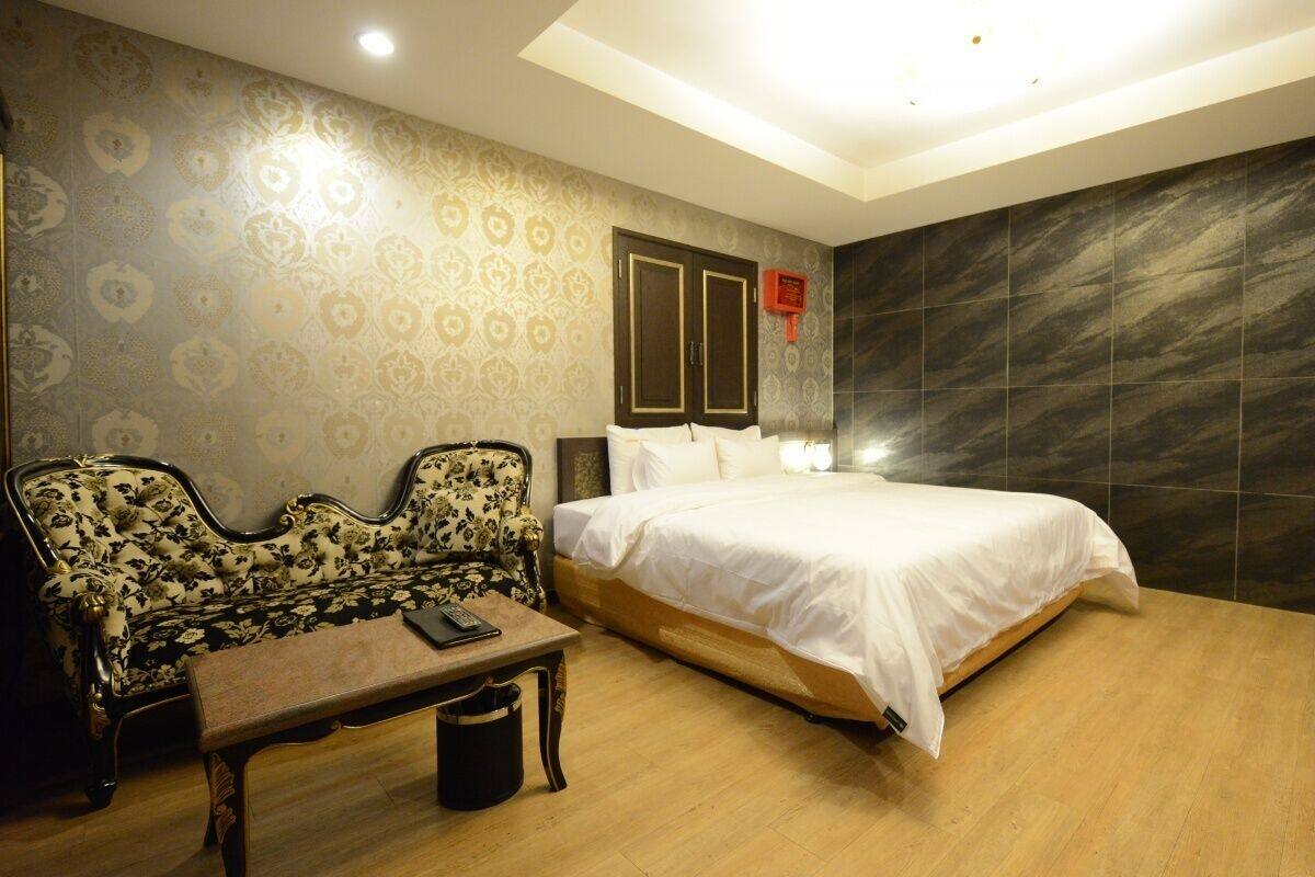 A bedroom with a bed, a sofa, a table, and a wall with a patterned design.