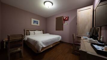 A bedroom with a bed, a desk with a computer, a chair, and a window with blinds.