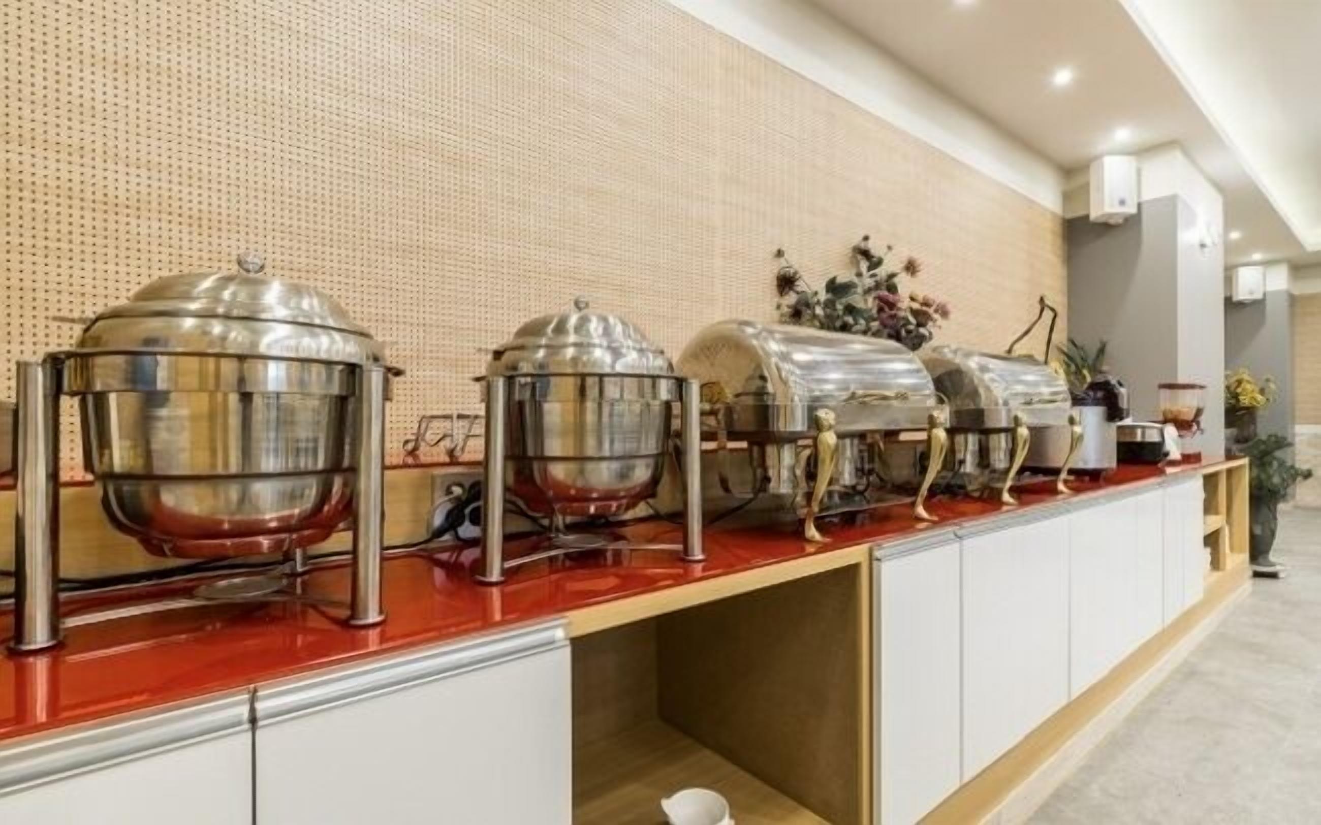 A buffet setup with multiple food dispensers on a red countertop, white cabinets below, and a textured wall in the background.