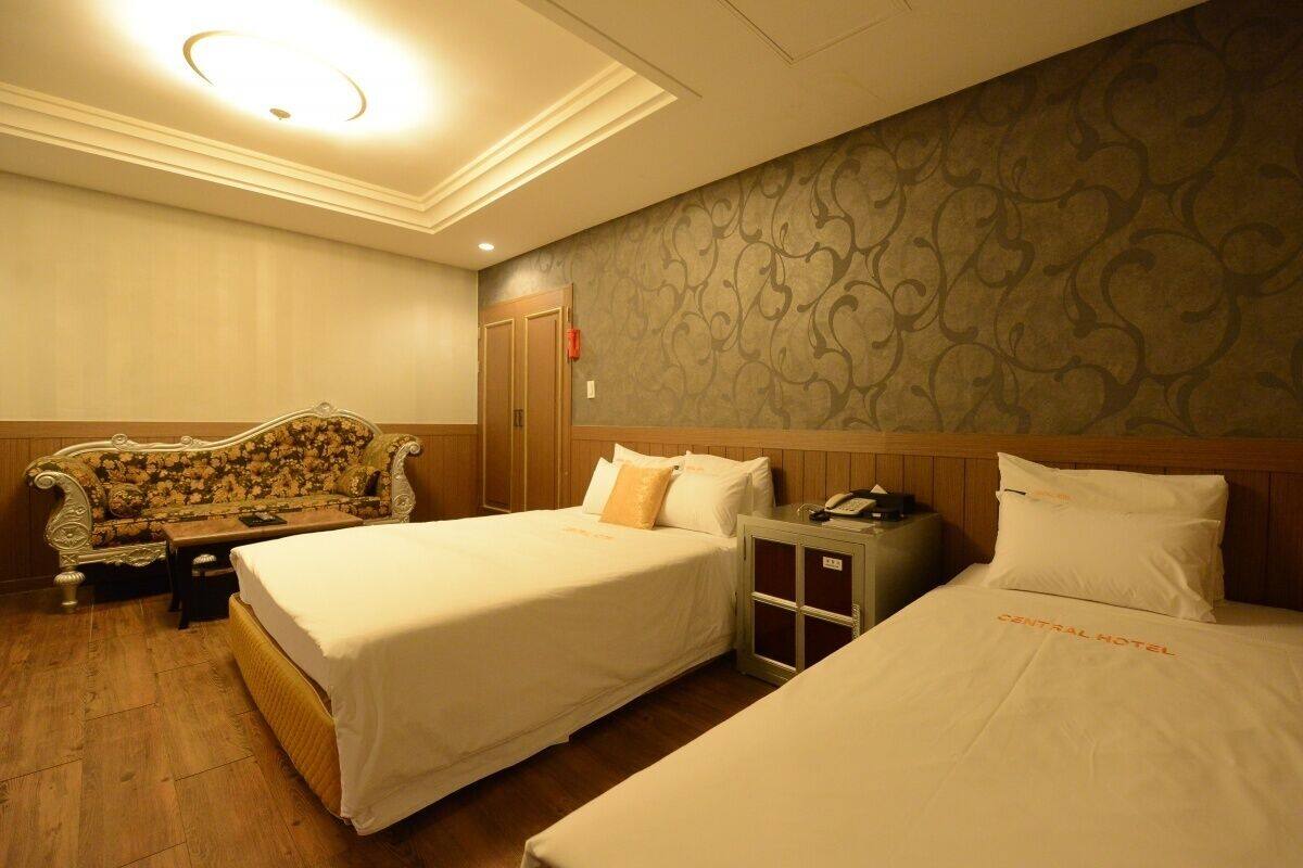 A hotel room with two single beds, a sofa, a nightstand, and a patterned wallpaper.