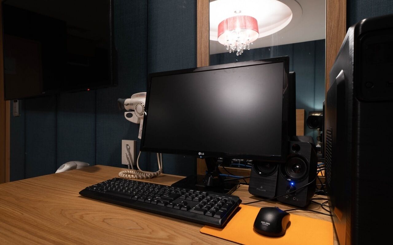 Een computeropstelling met een beeldscherm, toetsenbord, muis en speakers op een houten bureau.
