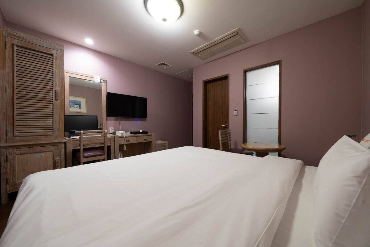 A hotel room with a bed, a desk with a chair, a television, and a wardrobe.