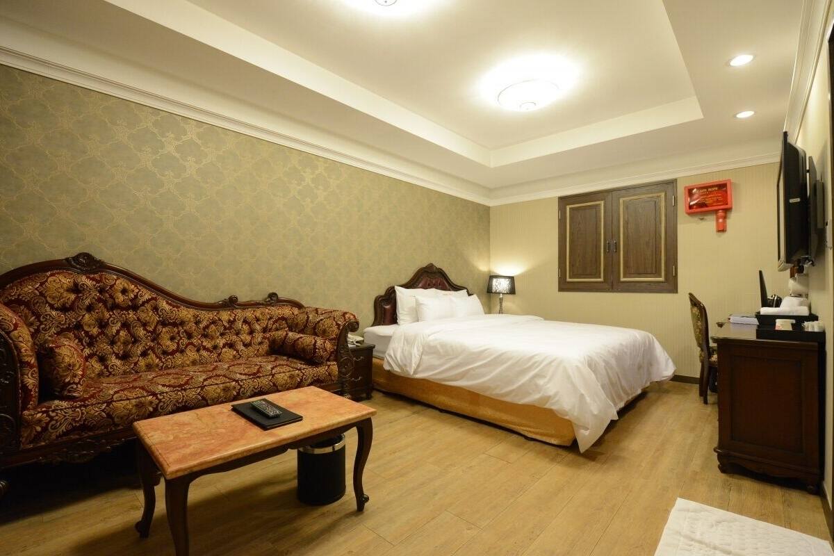 A hotel room with a large bed, a sofa, a small table, and a television.