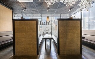 Uma sala de conferências moderna e minimalista, com divisória de vidro, uma mesa comprida e dois taburetes altos.
