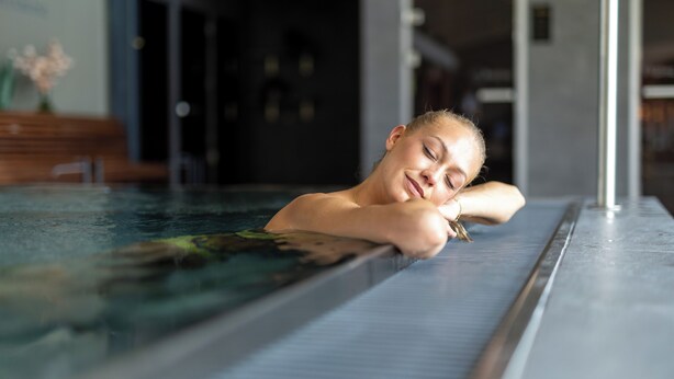 Une personne se détend dans une piscine intérieure moderne, dont les murs sont en verre transparent.