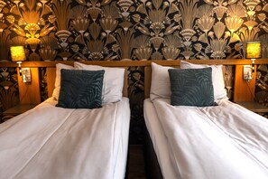 Un lit double avec une literie blanche et des coussins turquoise, placé devant un mur orné d’un papier peint à motifs floraux.