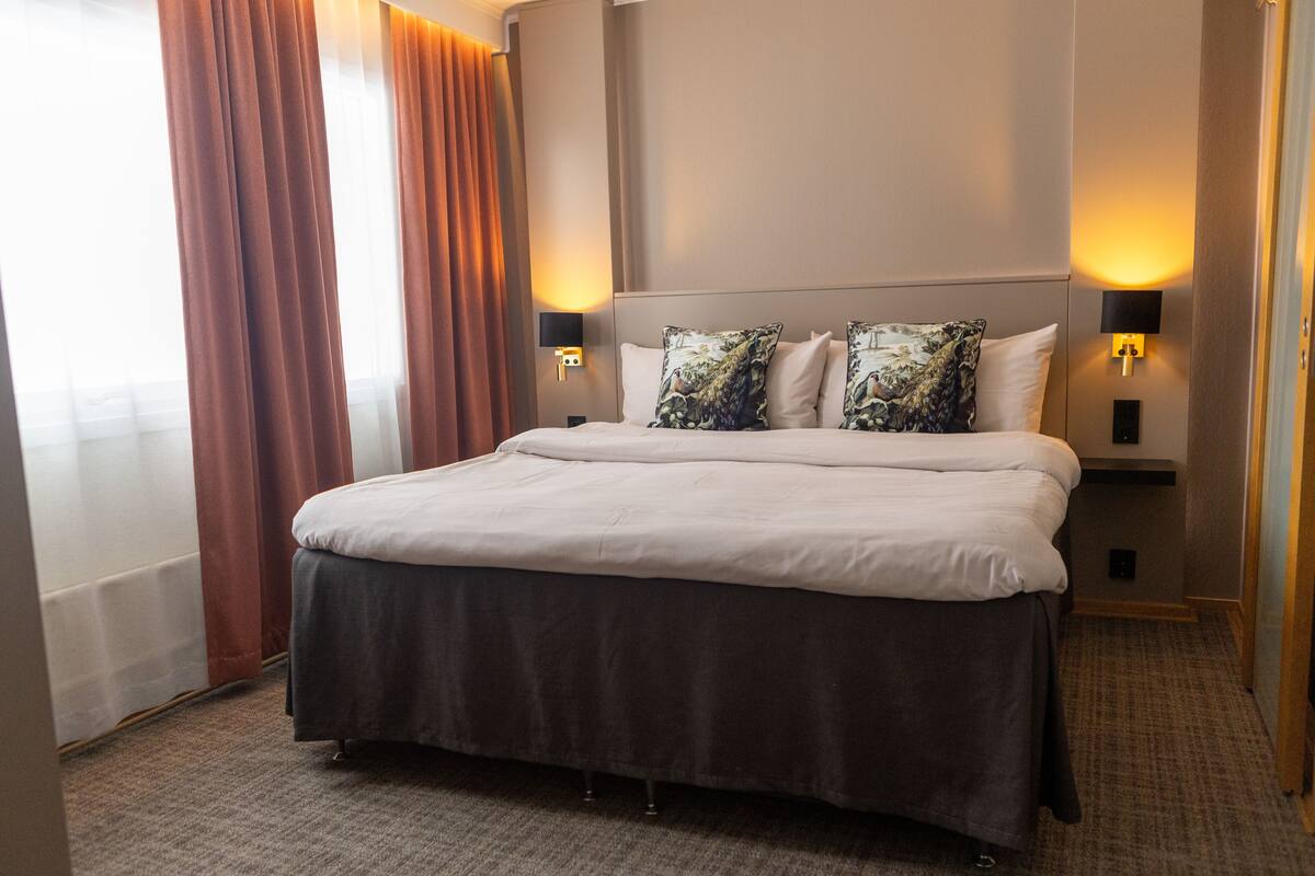 Ein Hotelzimmer mit einem großen Bett, zwei Wandlampen und einem mit Vorhängen versehenen Fenster.