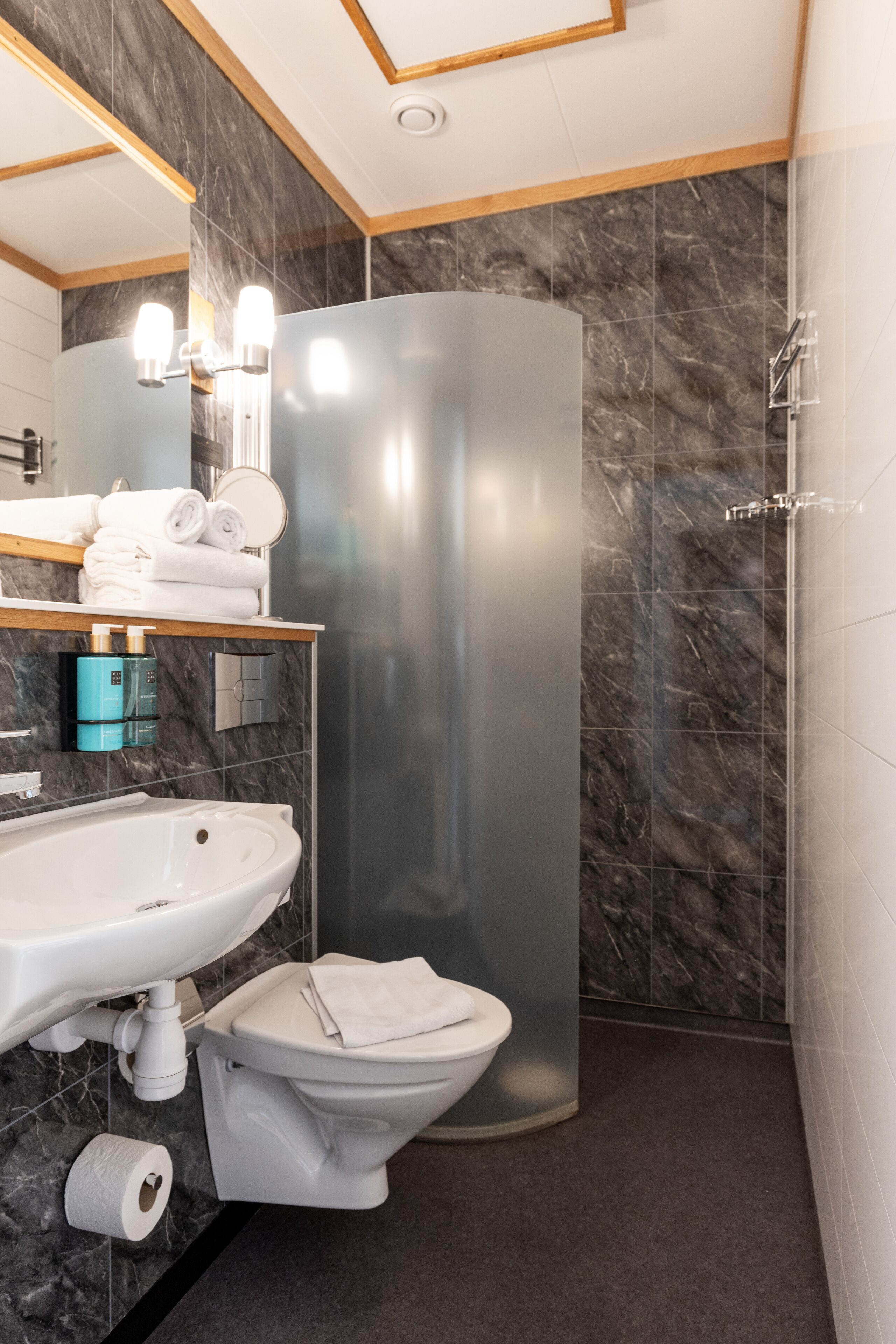 Une salle de bain moderne avec un pare-baignoire en marbre, un lavabo blanc, des toilettes et une cabine de douche.