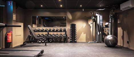 A gym with a treadmill, weight racks, a large exercise ball, and a mirrored wall.