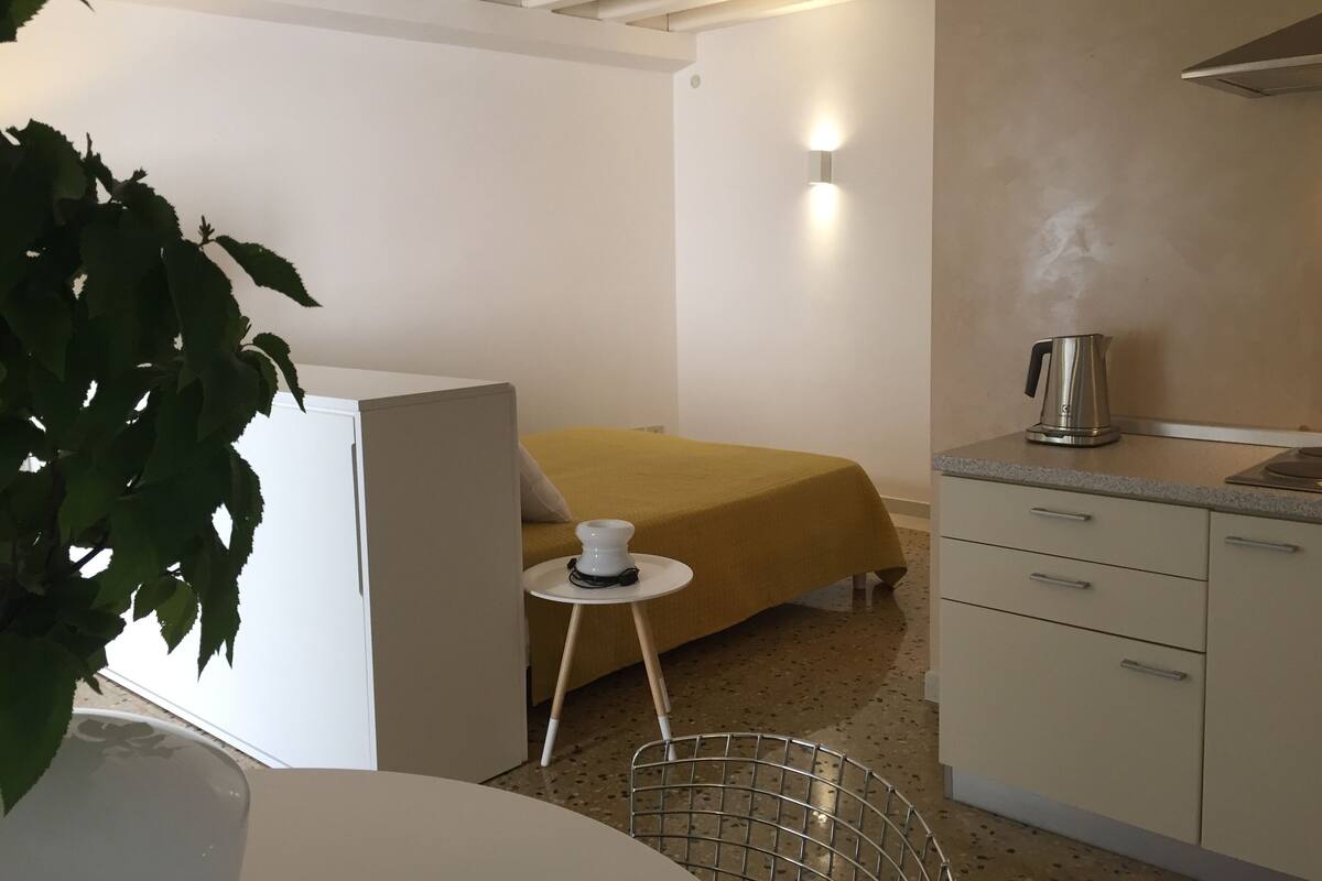 Habitación de hotel pequeña con cama, una mesita con una taza, hervidor en la encimera y una planta en maceta.