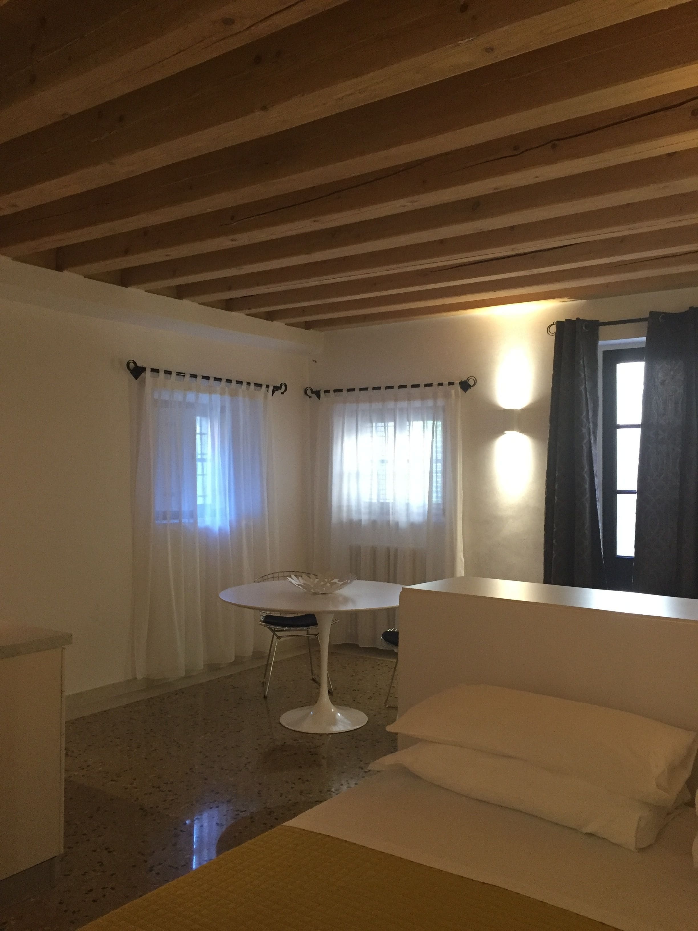 A room with a white table and chair, a white sofa, and a window with curtains.