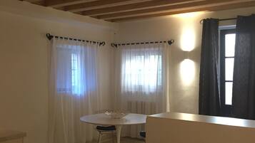 A room with a white table and chair, a white sofa, and a window with curtains.