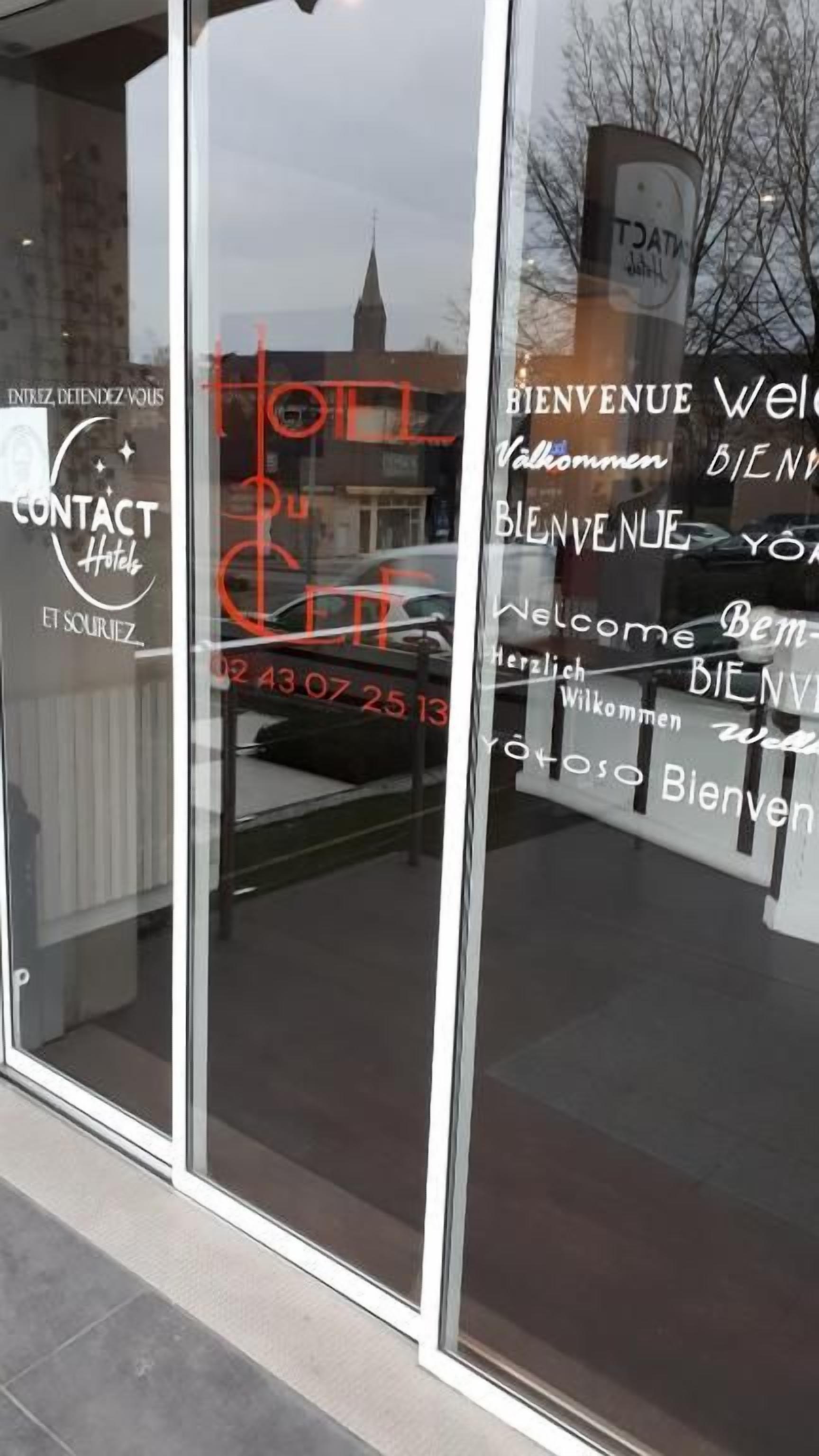 A hotel entrance with a glass door reflecting the sky and a building in the background.