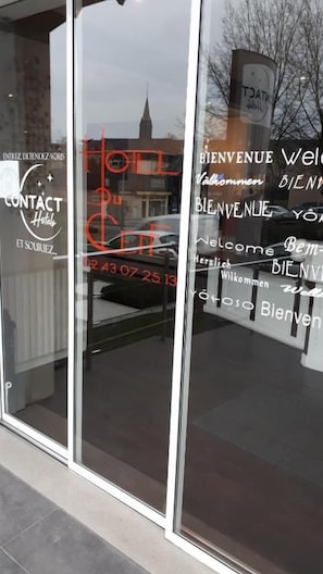 A hotel entrance with a glass door reflecting the sky and a building in the background. - Hôtel du Cerf (Château-Gontier-sur-Mayenne)