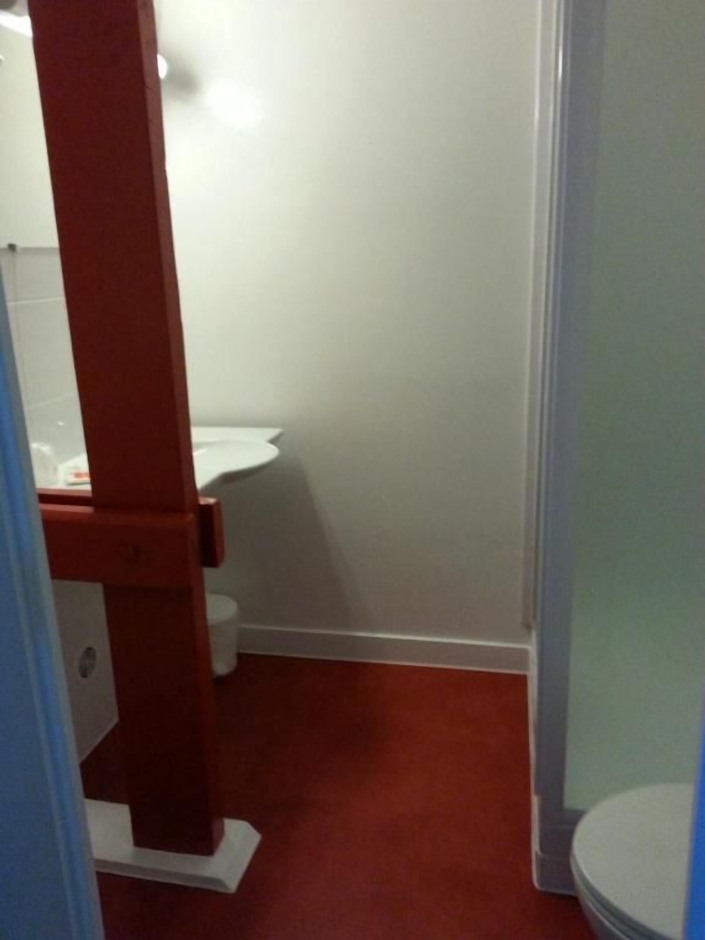 Un baño con inodoro blanco, estructura de madera y piso rojo.