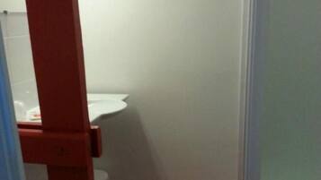 Un baño con inodoro blanco, estructura de madera y piso rojo.