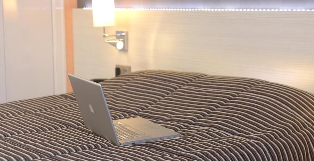A laptop on a bed with a striped bedspread.