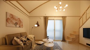 A modern living room with a sofa, a small round table, a flat-screen TV, and a staircase leading to an upper level. - Tribear House 2 (Seoul)