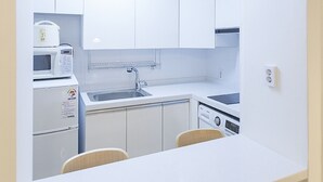 A compact kitchen with white cabinets, a microwave, a sink, and a stove. - Tribear House 2 (Seoul)