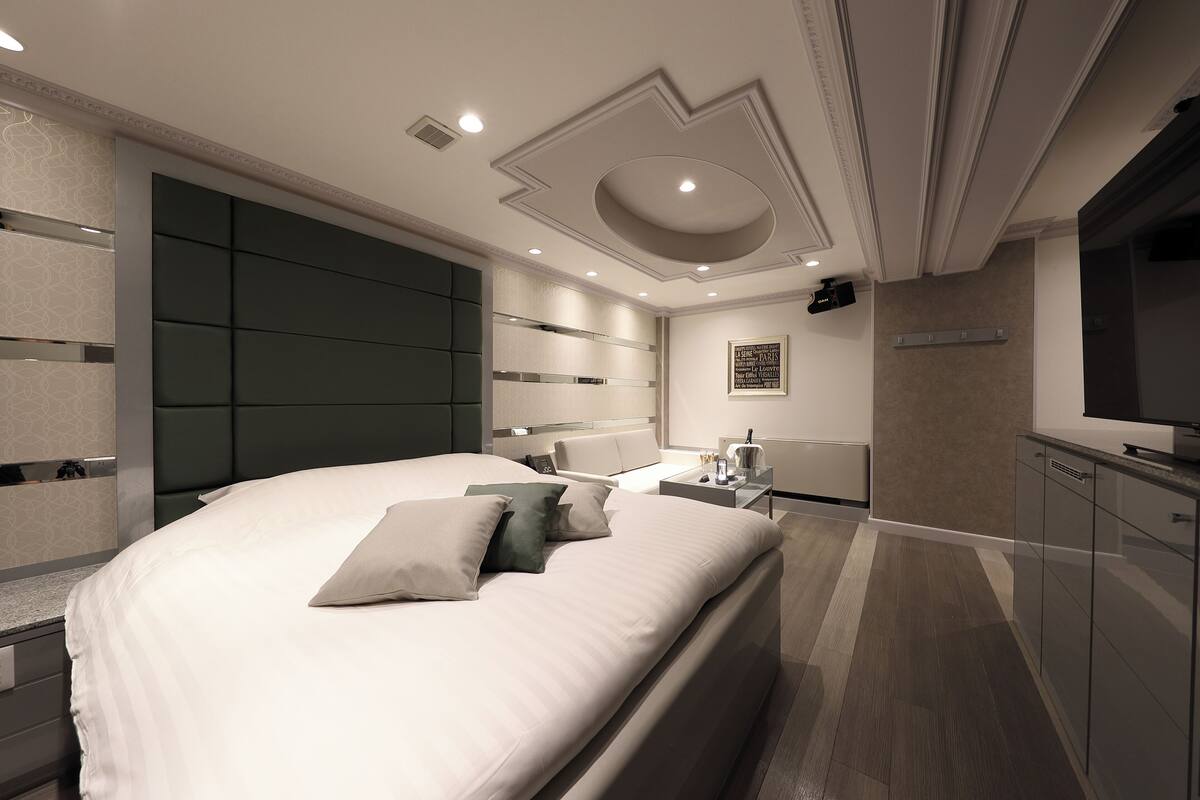 Un dormitorio moderno con una cama grande, cabecera integrada, mesitas de noche, un televisor de pantalla plana y una obra de arte colgada en la pared.