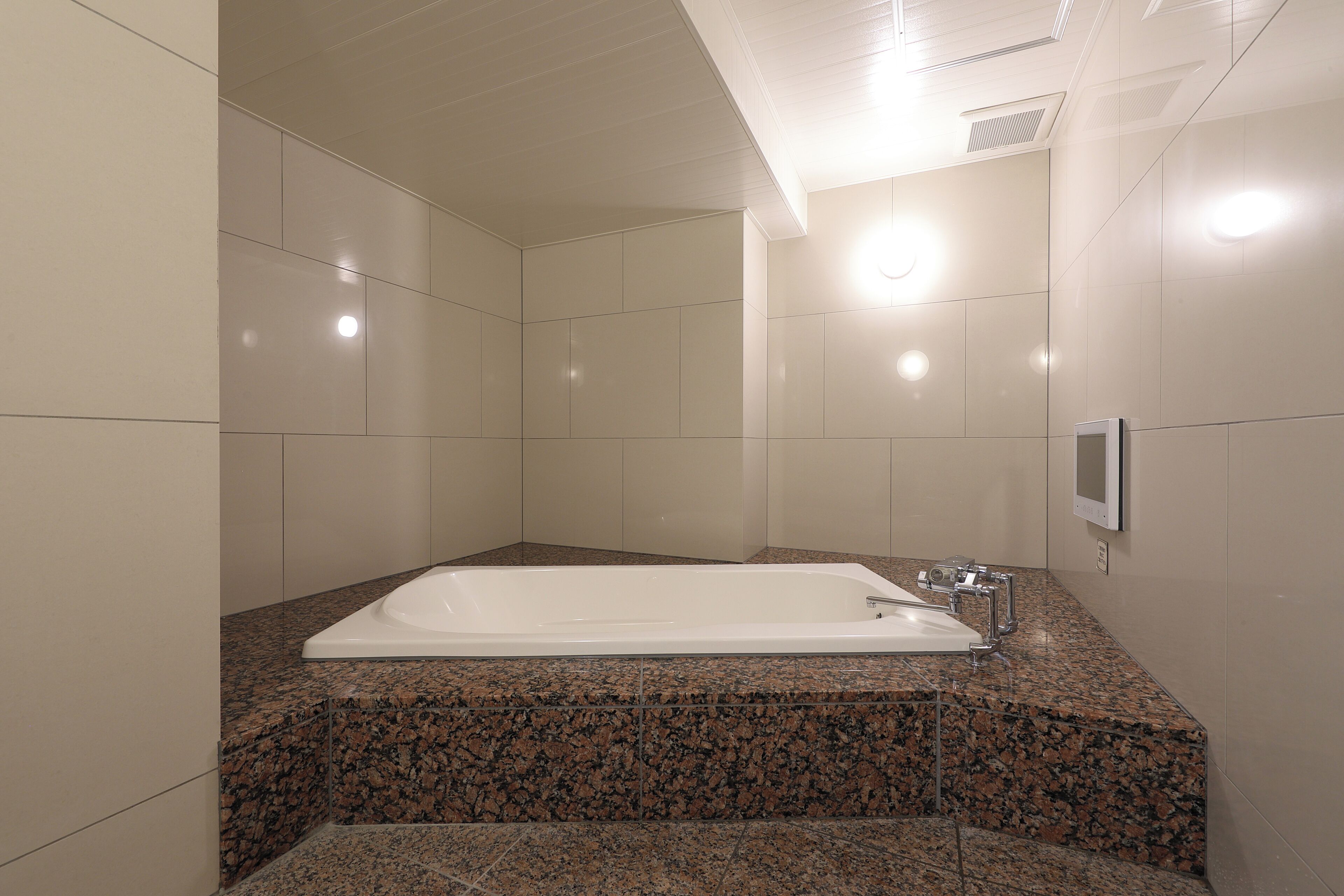 A modern bathroom with a large white bathtub, granite countertops, and a wall-mounted hand dryer.
