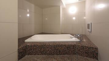 A modern bathroom with a large white bathtub, granite countertops, and a wall-mounted hand dryer.