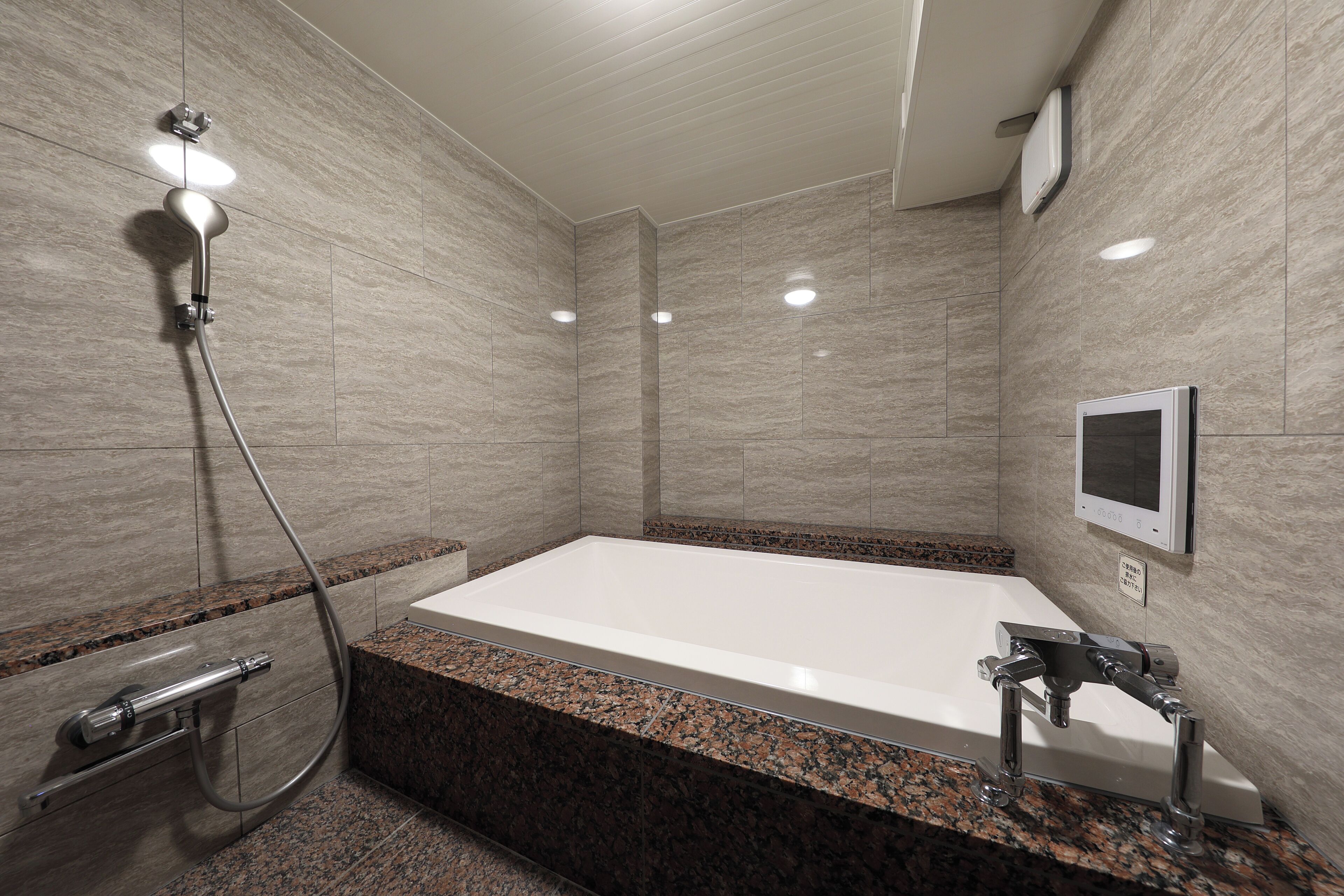 A modern bathroom with a large bathtub, a showerhead, and a built-in TV.