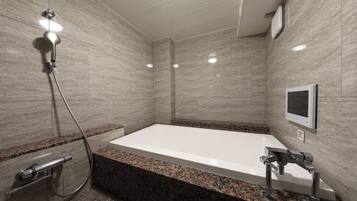 A modern bathroom with a large bathtub, a showerhead, and a built-in TV.