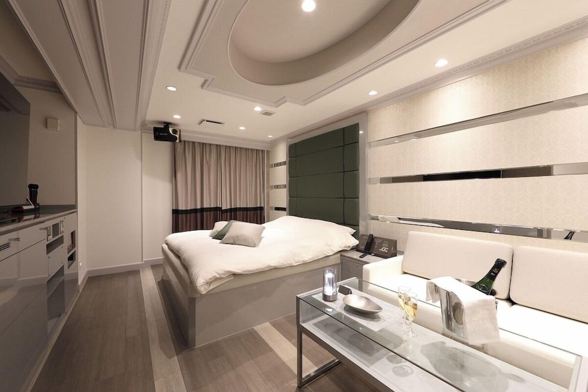 Une chambre d’hôtel moderne équipée d’un lit, d’une table basse en verre, d’un canapé et d’un mini-bar.