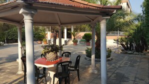 A covered outdoor seating area with a table and chairs, surrounded by potted plants and palm trees. - Villa Erry (Trani)