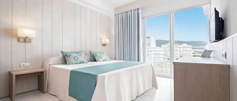 A hotel room with a large bed, a bedside table, a desk, and a view of the city through the window.