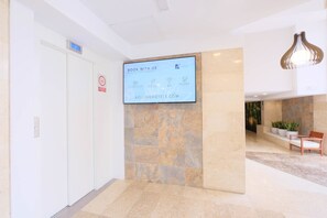 A hotel reception area with a digital screen displaying booking information, a white door, and a seating area with plants. - Azuline Palmanova Gardens (Calvia)