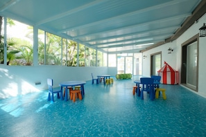 Un grand espace intérieur doté d’un sol carrelé de carreaux bleus, de nombreuses tables et chaises, et d’une maison de jeu.