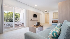 Una sala de estar moderna con un sofá, una mesa de centro y un televisor montado en la pared. Hay un ventanal corredero que da a un balcón con barandilla blanca.