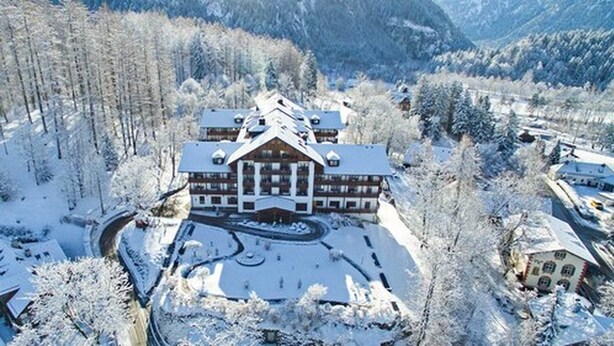 Ein großes Blockhaus mit mehreren Stockwerken und einem Innenhof, umgeben von schneebedeckten Bäumen und Bergen.