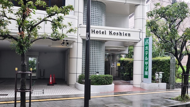 Hotel Koshien med en moderne facade, en flisebelagt indgang og et skilt, der angiver, at det er en del af Hotel Koshien-komplekset.