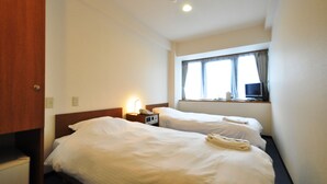 Et hotelværelse med to senge, et vindue med gardiner, et skrivebord med lampe og et fjernsyn.