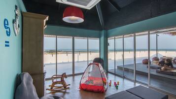 A room with a view of the beach, a rocking chair, a play tent, and a bench.