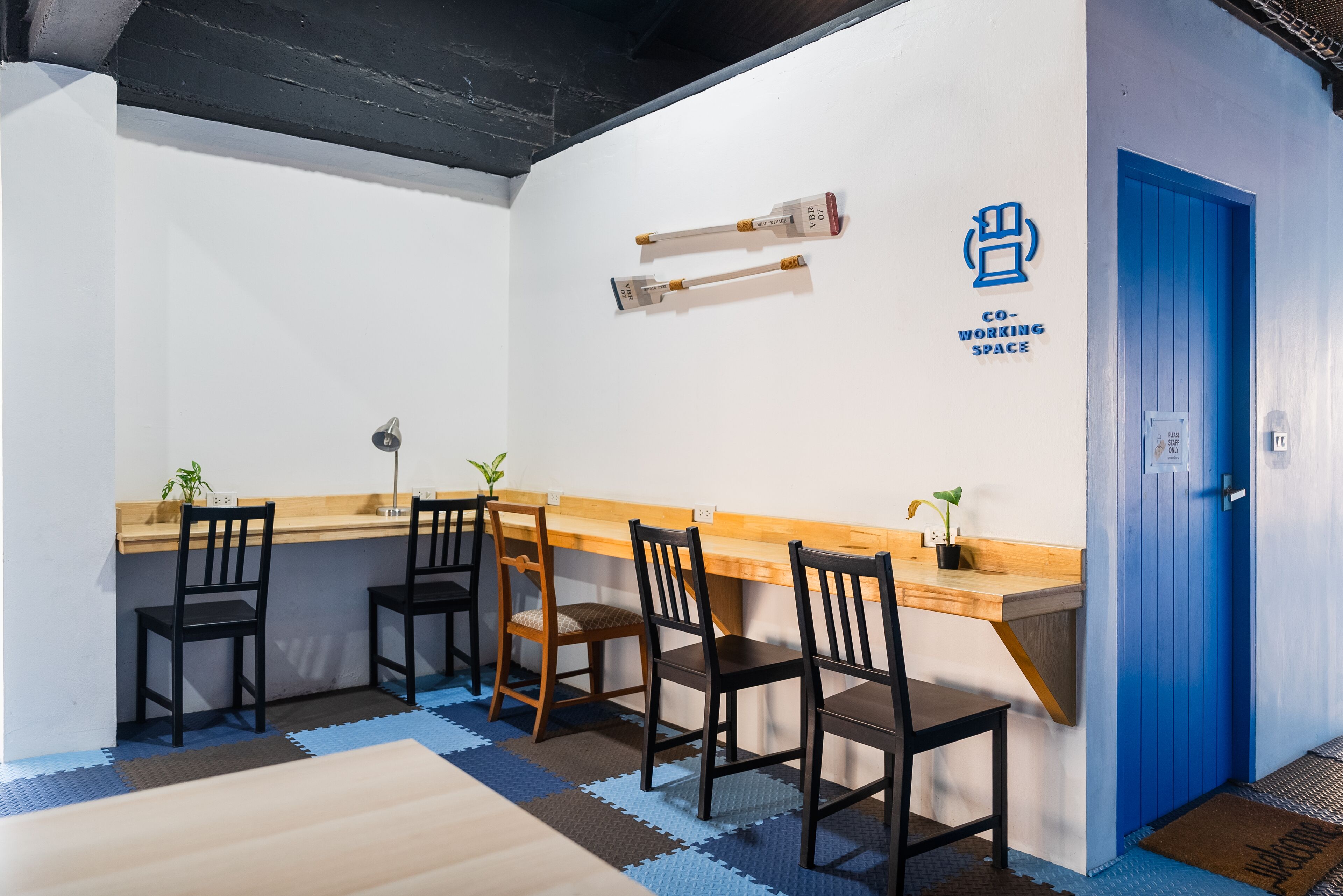 Un espacio de coworking con un escritorio de madera, cuatro sillas negras y una puerta azul.