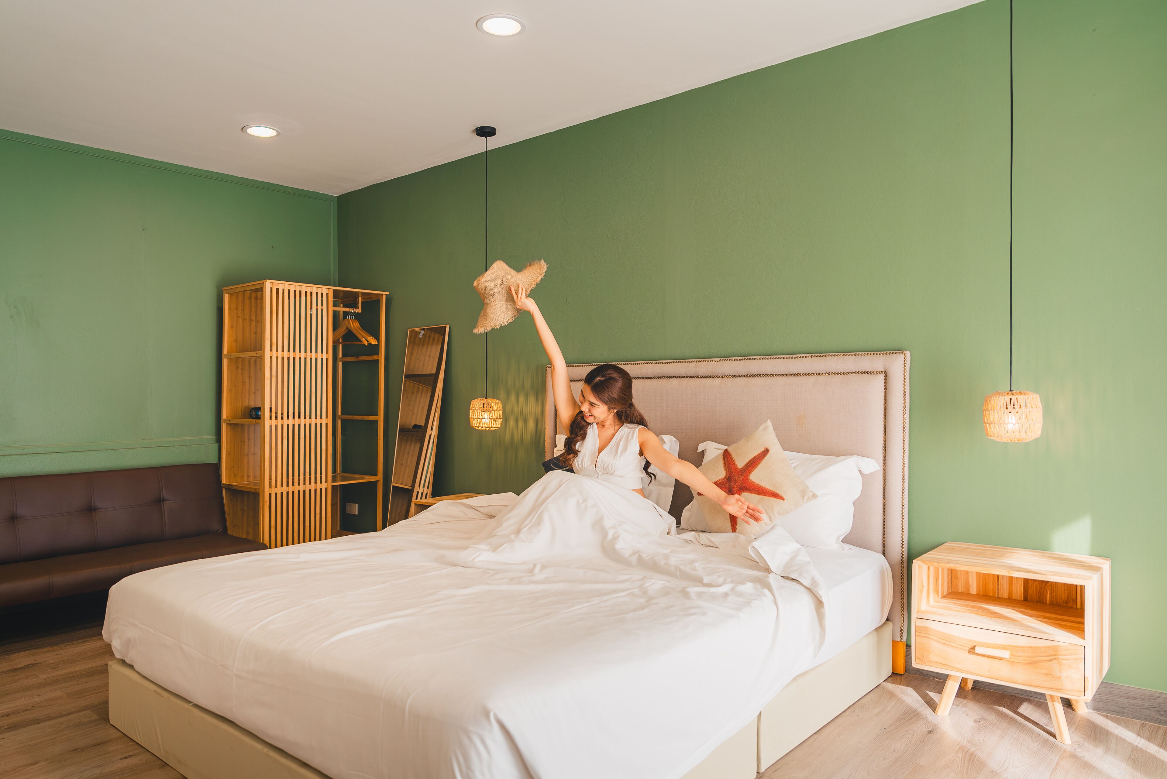 Una cama bien tendida con cabecera de madera, una mesita de noche y un armario en una habitación con paredes verdes y suelo de madera.