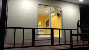Un bâtiment à l’extérieur jaune, doté d’une porte coulissante en verre et d’une terrasse en bois.