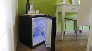 A compact refrigerator with a wine bottle and a glass on top, placed in a room with a green wall and a white chair.