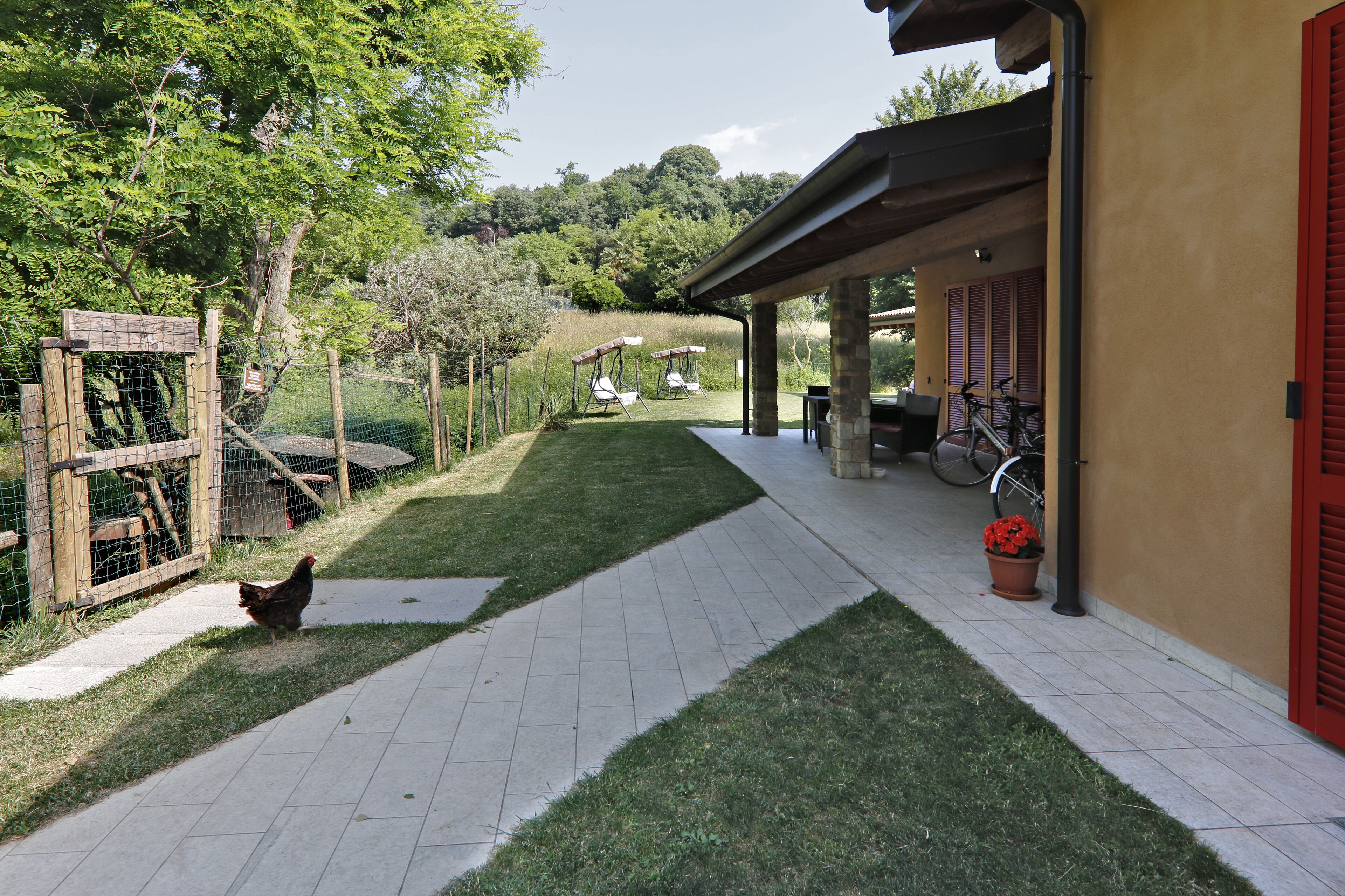 Un patio con zona de estar cubierta, un corral cercado para gallinas y un sendero de césped.