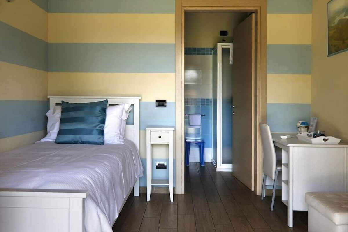 Een slaapkamer met een bed, nachtkastje, stoel, bureau en een badkamer zichtbaar door een geopende deur.