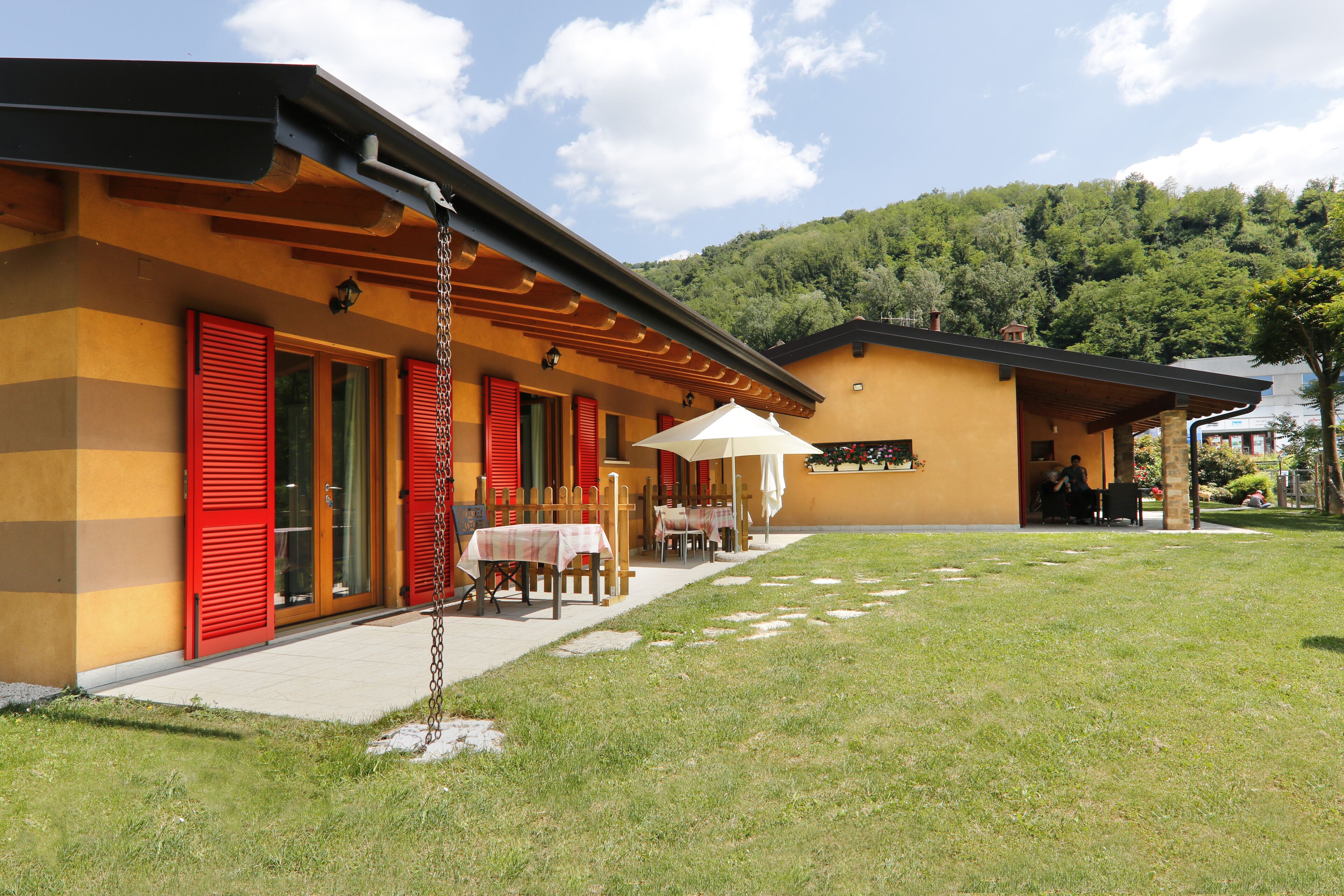A building with a covered outdoor seating area, a grassy lawn, and a mountain in the background.