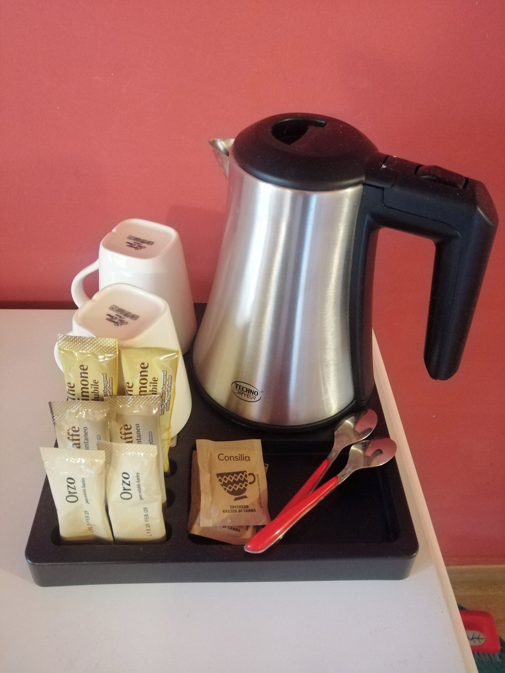A coffee maker, two white cups, and several packets of Orzo and Consilia on a tray.