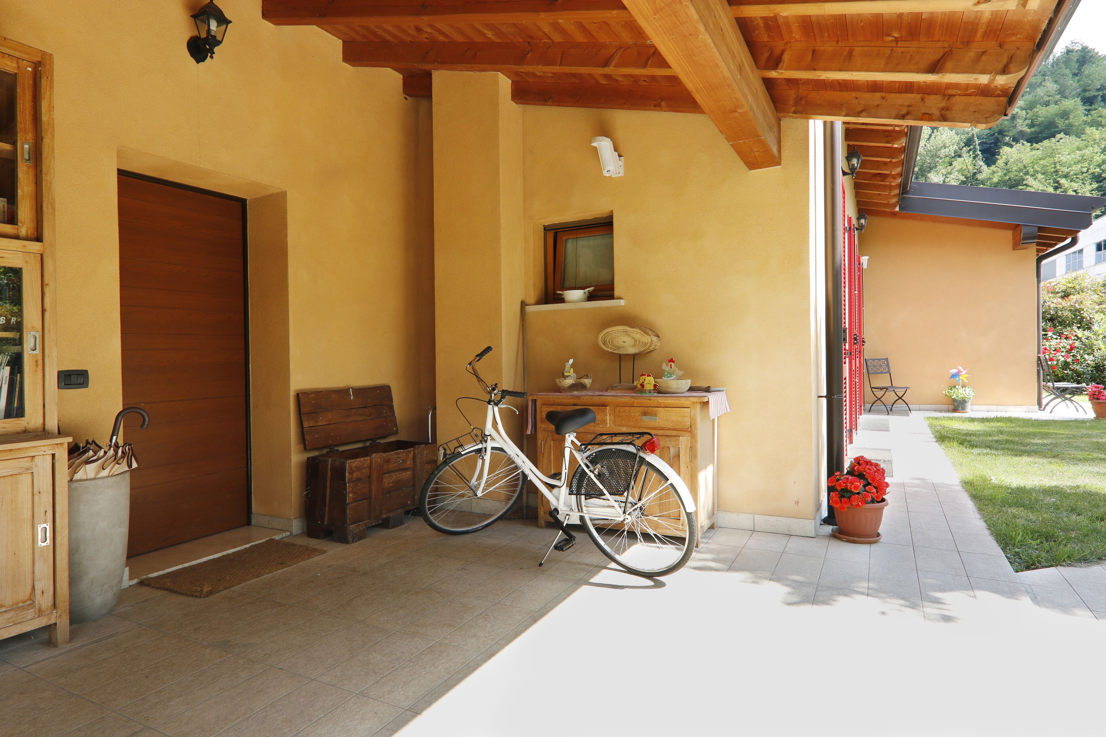 A wooden porch with a bicycle, a wooden cabinet, and a red door.