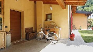 A wooden porch with a bicycle, a wooden cabinet, and a red door.